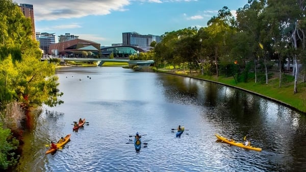 Estudiantes de la Golden Grove High School reman en kayaks y canoas por un tranquilo camino de agua con un moderno paisaje urbano.