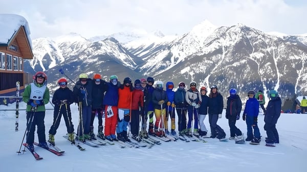 Un grupo de estudiantes de la Golden Secondary School está vestido para el invierno en una pendiente cubierta de nieve frente a un paisaje montañoso.