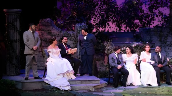 Una ceremonia de boda formal se lleva a cabo en el terreno del Golden West College al aire libre frente a un fondo verde y violeta.