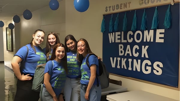 Estudiantes de la Gonzaga High School están sonriendo en el pasillo de la escuela frente a un banner de bienvenida con globos azules.