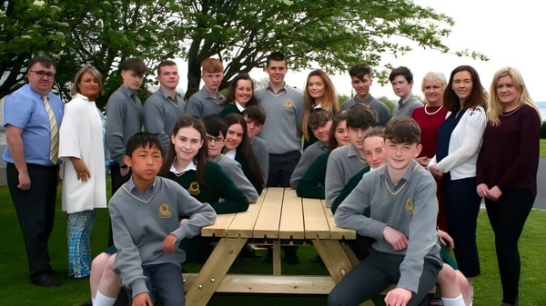 Un grupo de estudiantes está sentado alrededor de una mesa de madera al aire libre en el campus de la Gortnor Abbey School.
