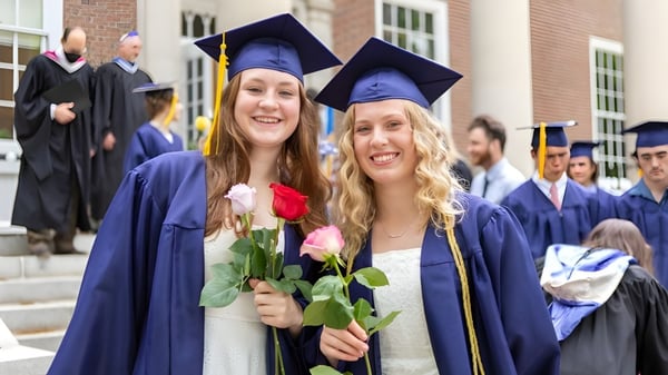 Dos graduadas de la Gould Academy están juntas con flores frente a un edificio de ladrillo.
