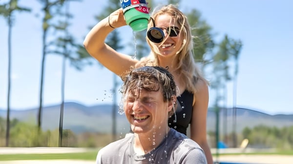 Una mujer rocía juguetonamente agua en la cara de un hombre en el campus de la Gould Academy al aire libre.