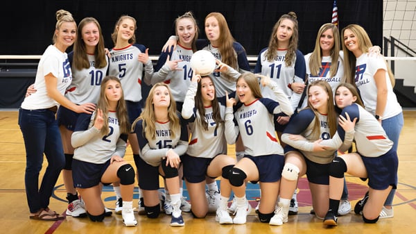 Un grupo de jóvenes jugadoras de volleyball de la Grace Academy posan juntas en una cancha de baloncesto.