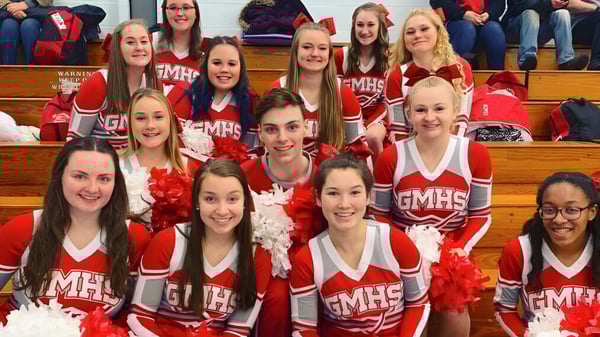 Un grupo de animadoras en uniformes rojos y blancos posan con pompones en el gimnasio de la Grand River Academy.