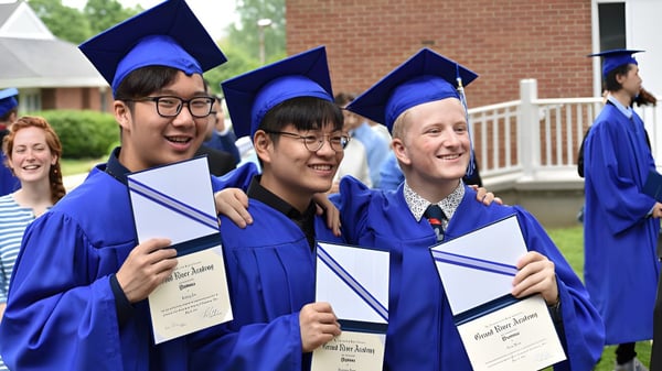 Un grupo de graduados de la Grand River Academy está con sombreros y togas azules frente a un edificio de ladrillo y sostiene sus diplomas.