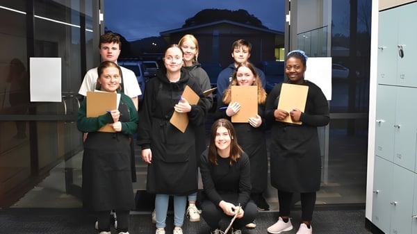Un grupo de estudiantes está de pie por la noche con carpetas frente a un edificio en el terreno de Grant High School.