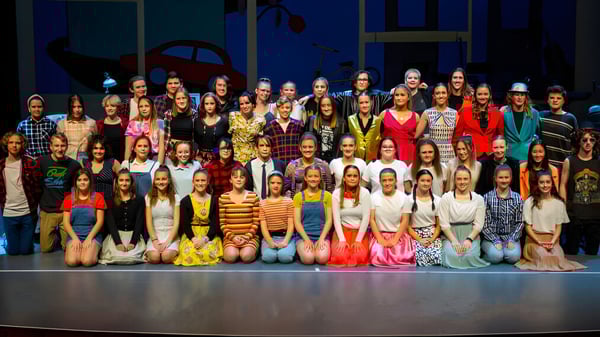 Un grupo de estudiantes se reúne en el escenario de Grant High School frente a un fondo oscuro.