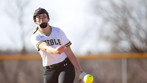 Un estudiante del Green Bay Area Public School District está de pie con un bate de béisbol y un casco en el campo de béisbol.