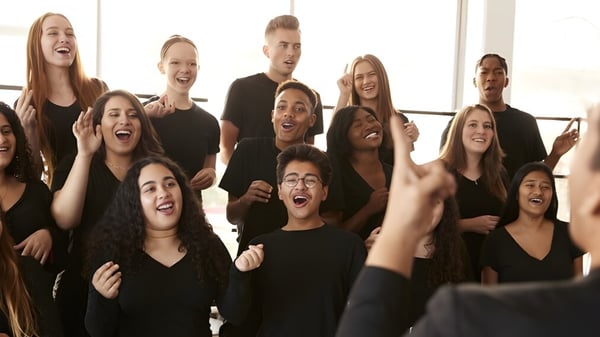 Estudiantes del Green Bay Area Public School District celebran juntos en una sala de ensayo con grandes ventanas.