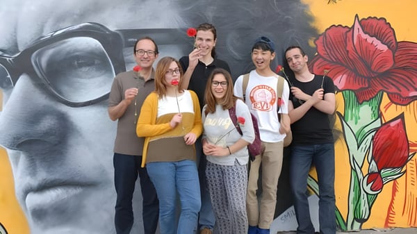 Un grupo de jóvenes adultos está frente a un colorido mural de flores en el campus de Greene's College Oxford.