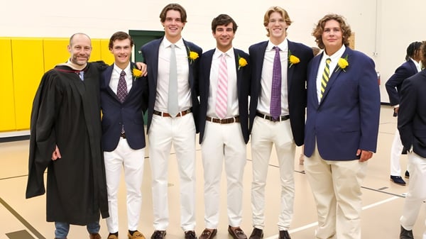 Un grupo de jóvenes estudiantes de Greensboro Day School está vestido formalmente frente a una pared amarilla en la escuela.