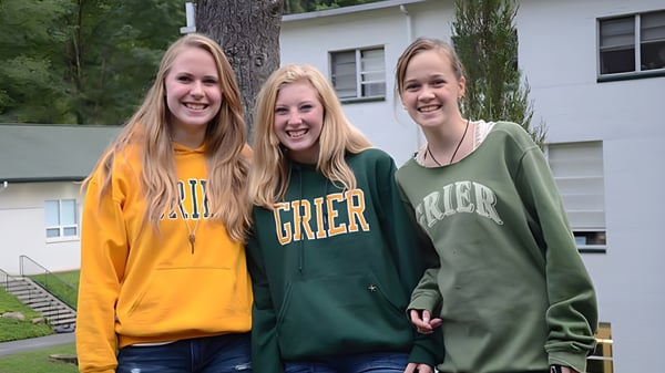 Tres alumnas de la Grier School están juntas frente a un edificio residencial y sonríen.
