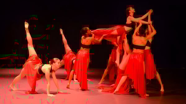 Alumnos y alumnas de la Grier School realizan una actuación de danza en el escenario con trajes rojos.