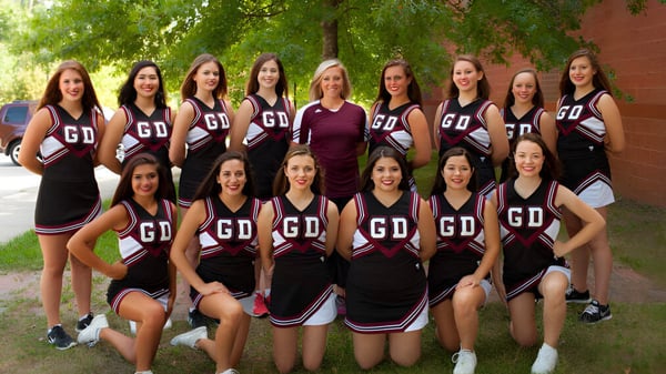 Un grupo de estudiantes de la Groton-Dunstable Regional High School está de pie juntos al aire libre en un área verde con árboles de fondo.