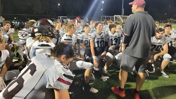 Un grupo de jóvenes futbolistas del Groton-Dunstable Regional School District se reúne por la noche en el campo con un entrenador.