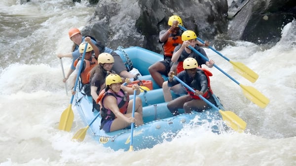 Un grupo de estudiantes de la Groton School realiza un tour de rafting en aguas bravas en una balsa azul en un paisaje rocoso.