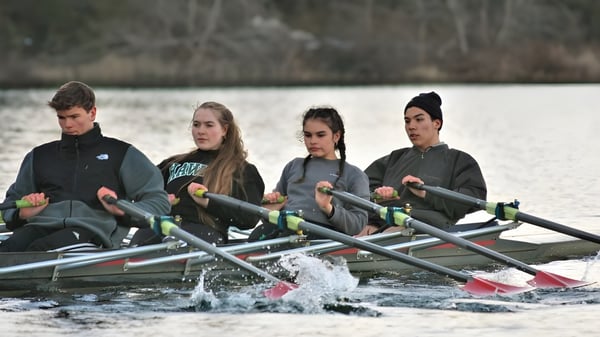 Cuatro estudiantes de la Gulf Islands Secondary School reman en un lago rodeado de bosque.