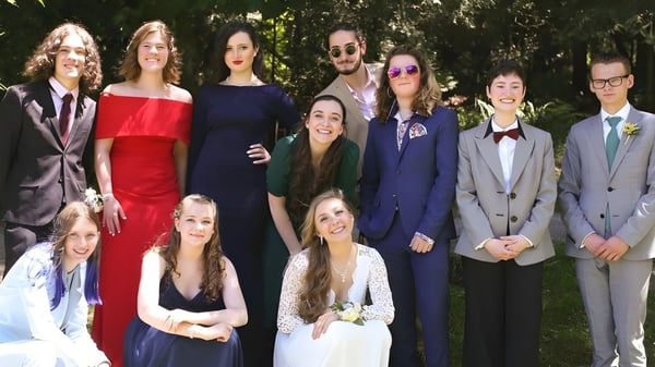 Un grupo de estudiantes de la Gulf Islands Secondary School posan con ropa formal al aire libre frente a árboles y vegetación.