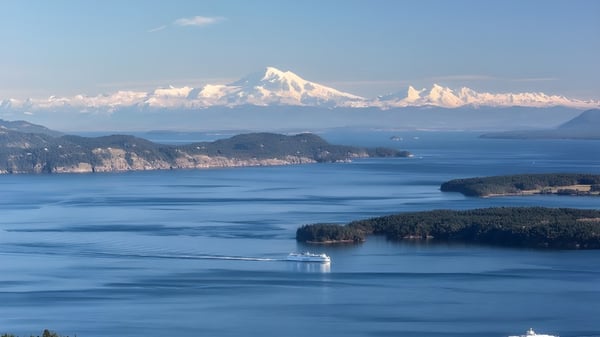 Vista de una superficie de agua tranquila con islas boscosas y montañas nevadas al fondo cerca de la Gulf Islands Secondary School.