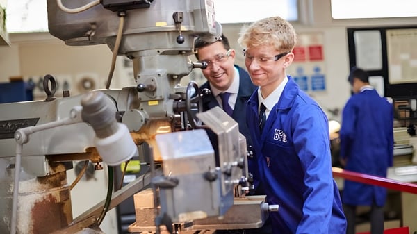 Dos estudiantes de Haberdashers' Monmouth Schools trabajan juntos en una gran máquina industrial en el taller.