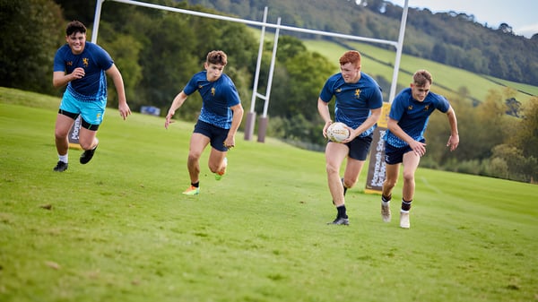 Estudiantes de Haberdashers' Monmouth Schools corren en un campo de juego en medio de colinas verdes y árboles.