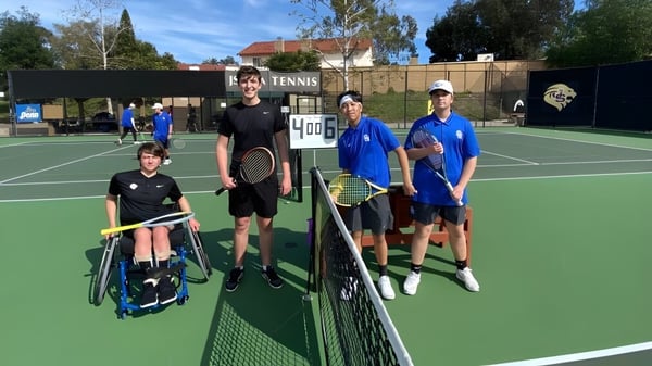 Estudiantes de la Hackett High School están en el campo de tenis frente a la red durante una sesión de entrenamiento al aire libre.