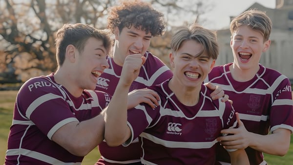 Un grupo de cuatro alumnos de la Haileybury School está en uniformes de rugby en un área boscosa al aire libre.