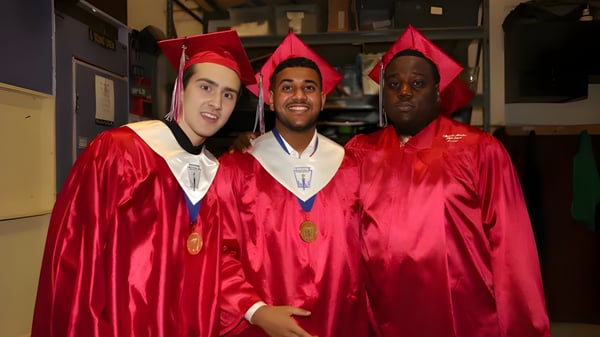Tres graduados en togas rojas están juntos en el pasillo de la Hamilton Boy's High School.