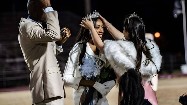 Una mujer con corona y abrigo de piel en una celebración en la Hamilton Christian Academy con dos mujeres más.