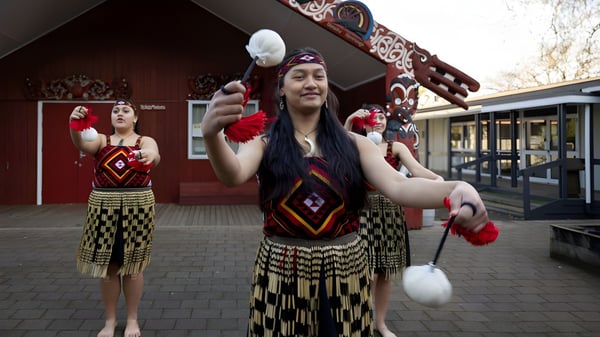 Dos alumnas de la Hamilton Girl's High School llevan vestimenta tradicional maorí frente a un edificio destacado de la escuela.