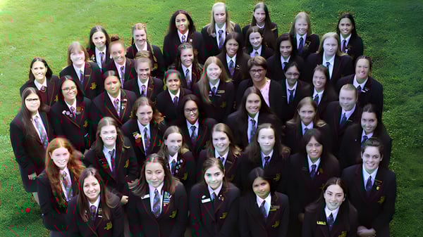 Un gran grupo de alumnas de la Hamilton Girl's High School está de pie en un campo cubierto de hierba.