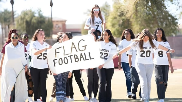 Un grupo de alumnas de Hamilton High School sostiene un cartel de Flag Football frente al campus escolar.
