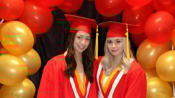 Dos graduadas de la Hammarskjold High School posan en sus vestidos de graduación frente a globos rojos y dorados.