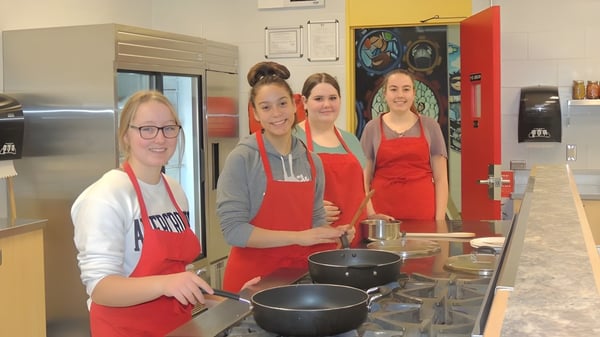 Cuatro estudiantes de la Hammarskjold High School están en una cocina preparando comida juntas.