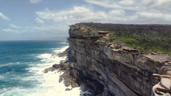 Vista de un acantilado rocoso con densa vegetación y el mar turquesa de fondo en el terreno de Hampton Senior High School.