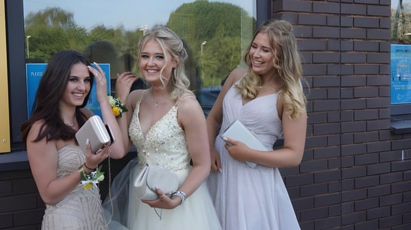 Tres estudiantes de la Hanham Woods Academy están en ropa formal frente a un edificio de ladrillo con plantas verdes.