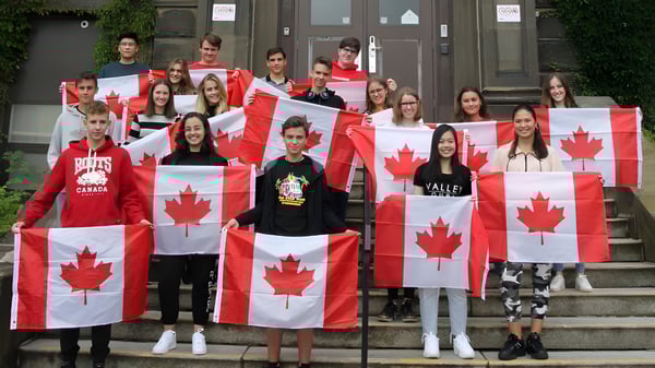 Estudiantes de la Harbour View High School están en las escaleras de un edificio sosteniendo grandes banderas canadienses.