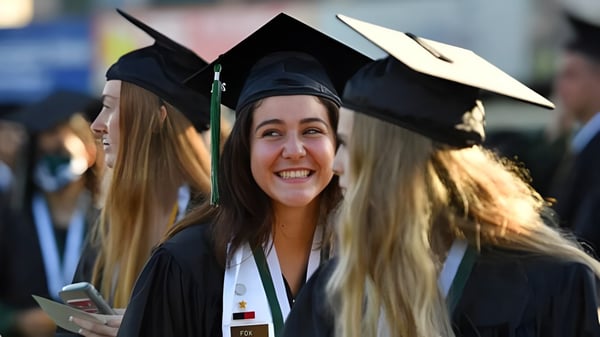 Una graduada sonriente en toga está con otros graduados en el terreno de la Harbour View High School.