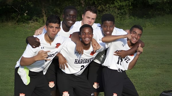 Un grupo de estudiantes en uniformes deportivos se abraza y sonríe en un campo de césped de la Hargrave Military Academy.