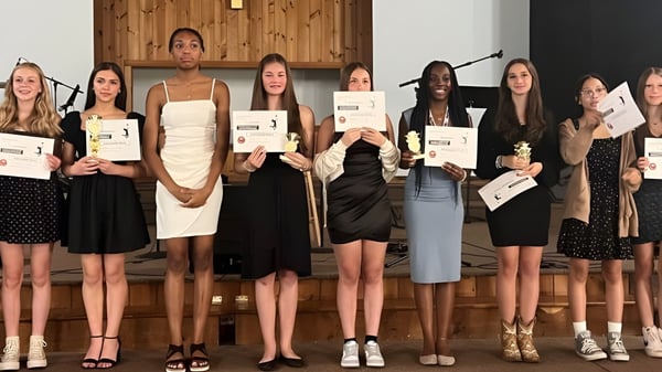 Un grupo de estudiantes de la Harmony Christian School sostiene en una sala de madera cada uno un certificado en la mano.