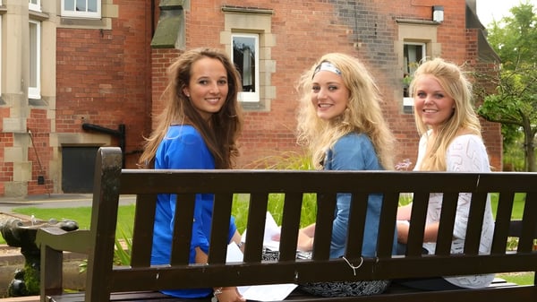 Tres alumnas están en un balcón de madera frente a un edificio de ladrillo en el campus del Harrogate Ladies’ College.