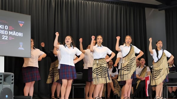 Alumnas de Hastings Girls' High School realizan un baile en un escenario vestidas con ropa tradicional maorí.