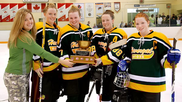 Alumnas del Havergal College sostienen un trofeo en una sala de hockey con banderas canadienses.