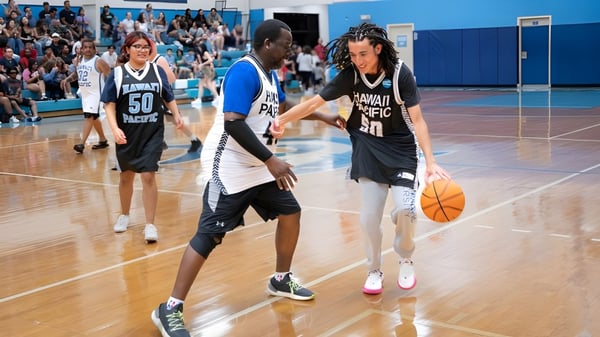 Dos jugadores de baloncesto de la Hawai'i Pacific University driblan en la cancha frente a los espectadores.