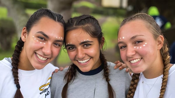 Tres alumnas de la Hawaii Preparatory Academy sonríen juntas y posan al aire libre frente a los árboles y el verde.