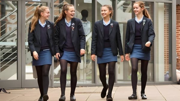 Cuatro alumnas de la Headington School están juntas frente a un edificio de vidrio y sonríen.