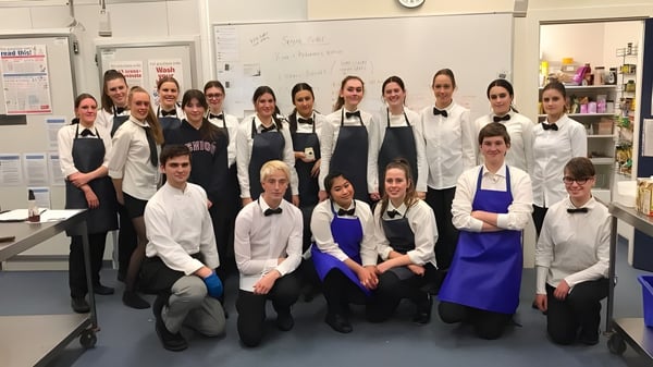Estudiantes de la Heathfield High School están en la cocina de la escuela en uniformes de cocina juntos.
