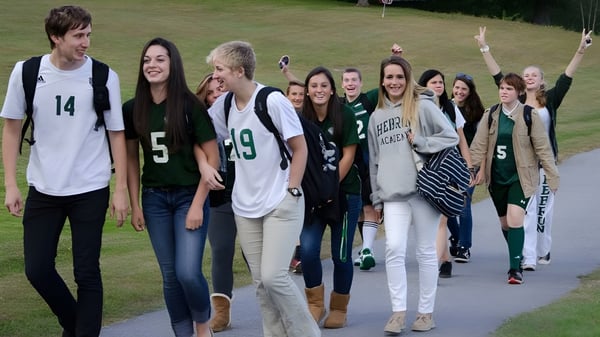 Un grupo de estudiantes está reunido en un campo de hierba en el campus de la Hebron Academy.