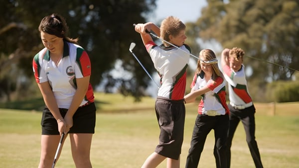 Un grupo de estudiantes en ropa deportiva está en un campo de deportes de la Henley High School bajo un cielo despejado.